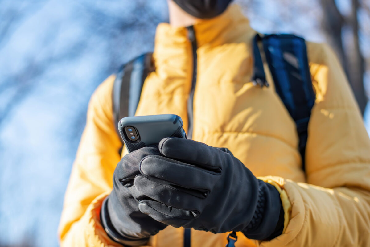 food delivery man with backpack using his smartphone yellow jacket and black gloves winter