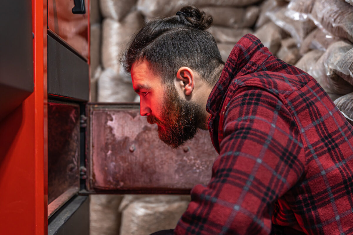 a man in a room with a solid fuel boiler working on biofuel economical heating